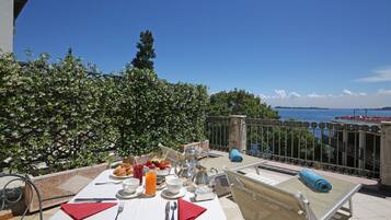 Mesa lista para el desayuno con vista al mar, una barandilla de metal y una toalla azul en una silla.
