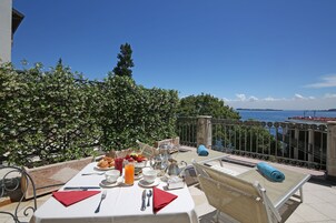 Mesa lista para el desayuno con vista al mar, una barandilla de metal y una toalla azul en una silla.