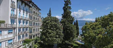 Un hôtel doté d’une piscine entourée de chaises longues et de parasols, offrant une vue dégagée sur la mer, et avec un grand arbre au premier plan.