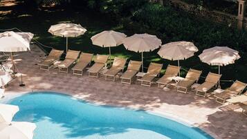 Ein Swimmingpool mit Liegestühlen und Sonnenschirmen, umgeben von Grünpflanzen.