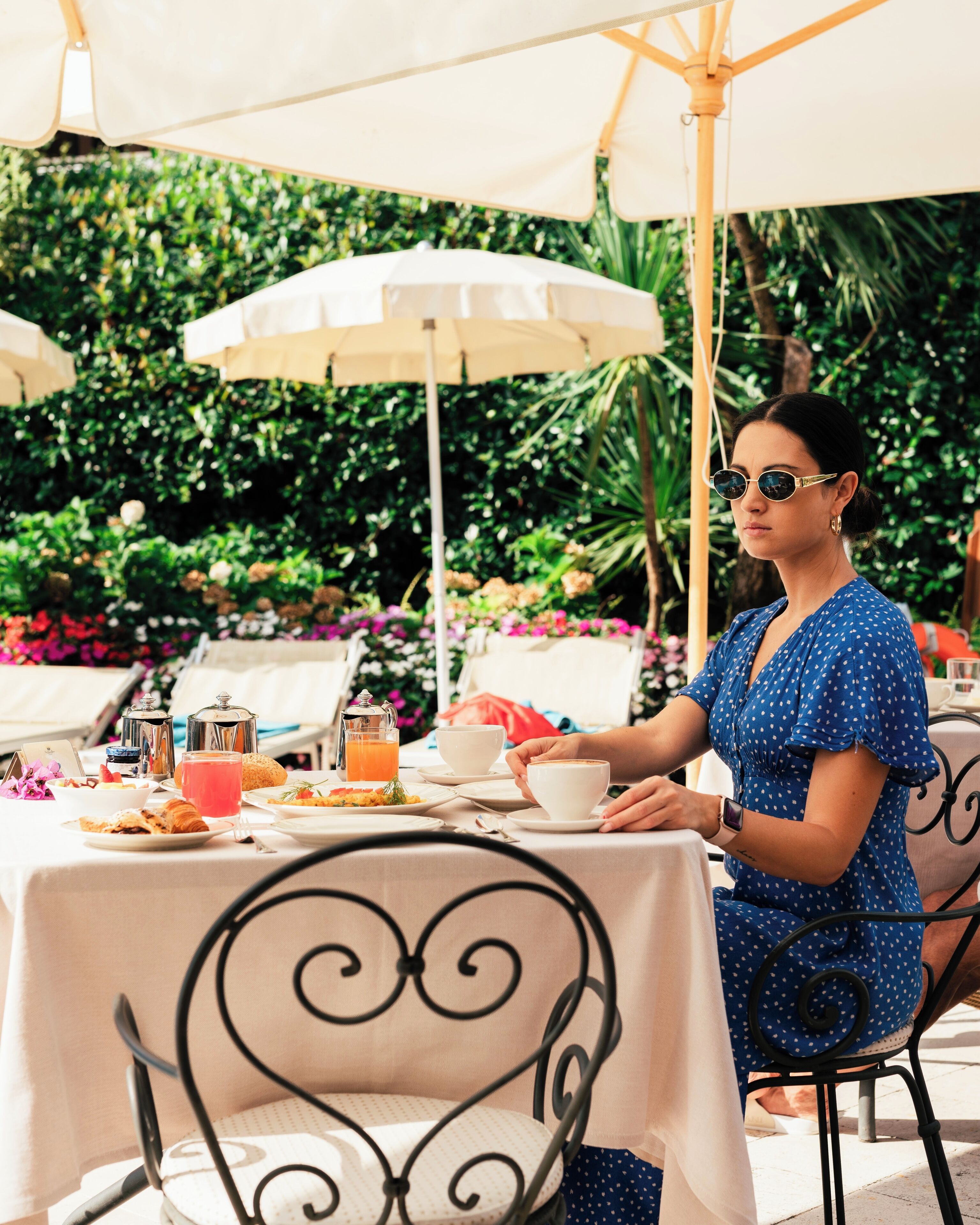 A dining table set outdoors with a person seated, surrounded by various dishes and drinks.