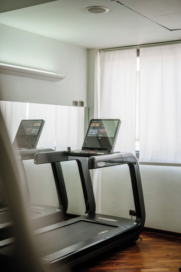 A treadmill and a laptop in a room with a wooden floor and a window with curtains.