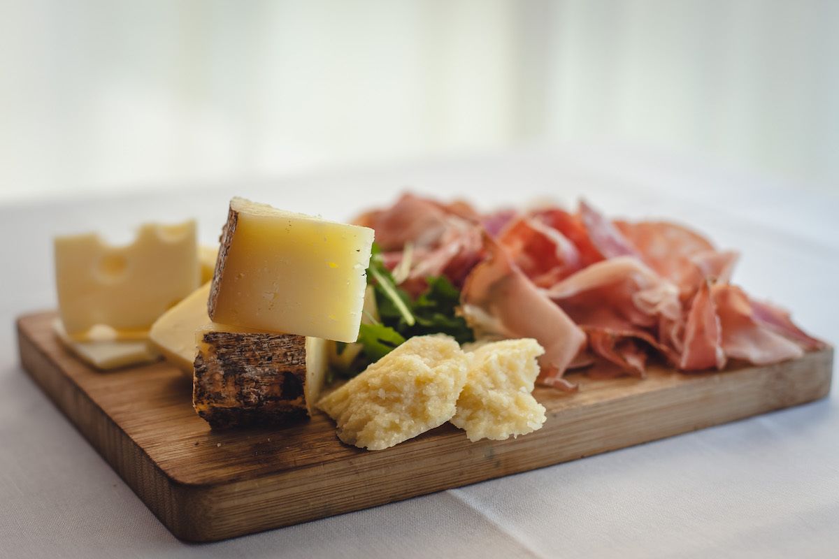 A wooden board with various cheeses, a piece of cured meat, and some greens.