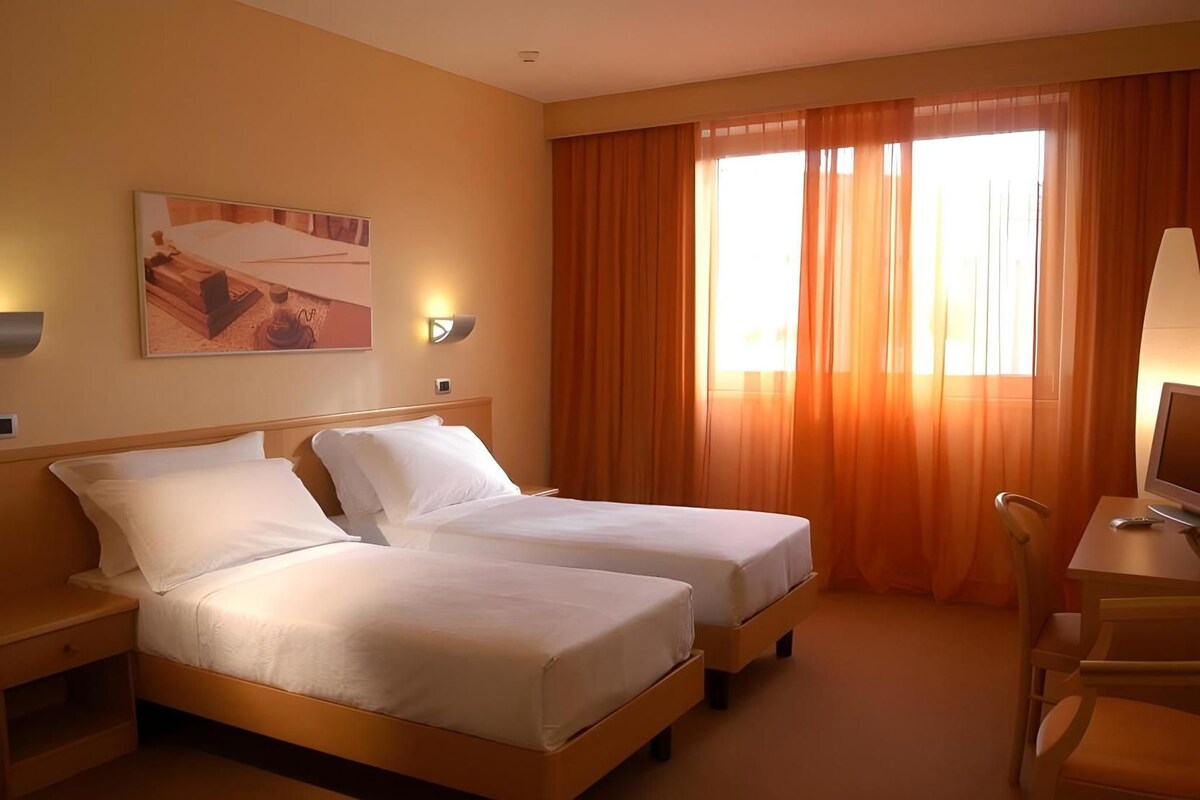 Habitación de hotel con dos camas, un escritorio con silla, televisor y un cuadro en la pared.