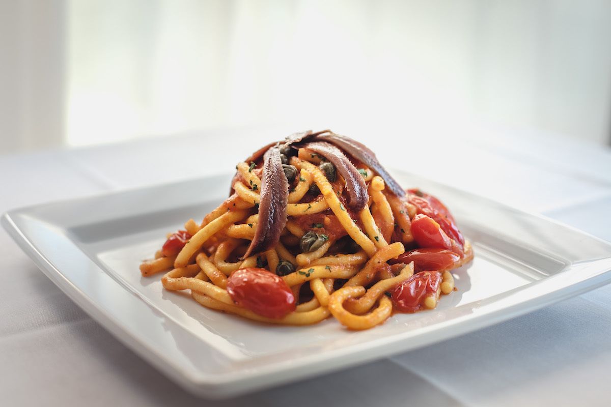 Un piatto di spaghetti con pomodori e capperi su un piatto bianco.
