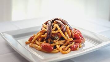 Un plato de espagueti con tomates y alcaparras sobre un plato blanco.