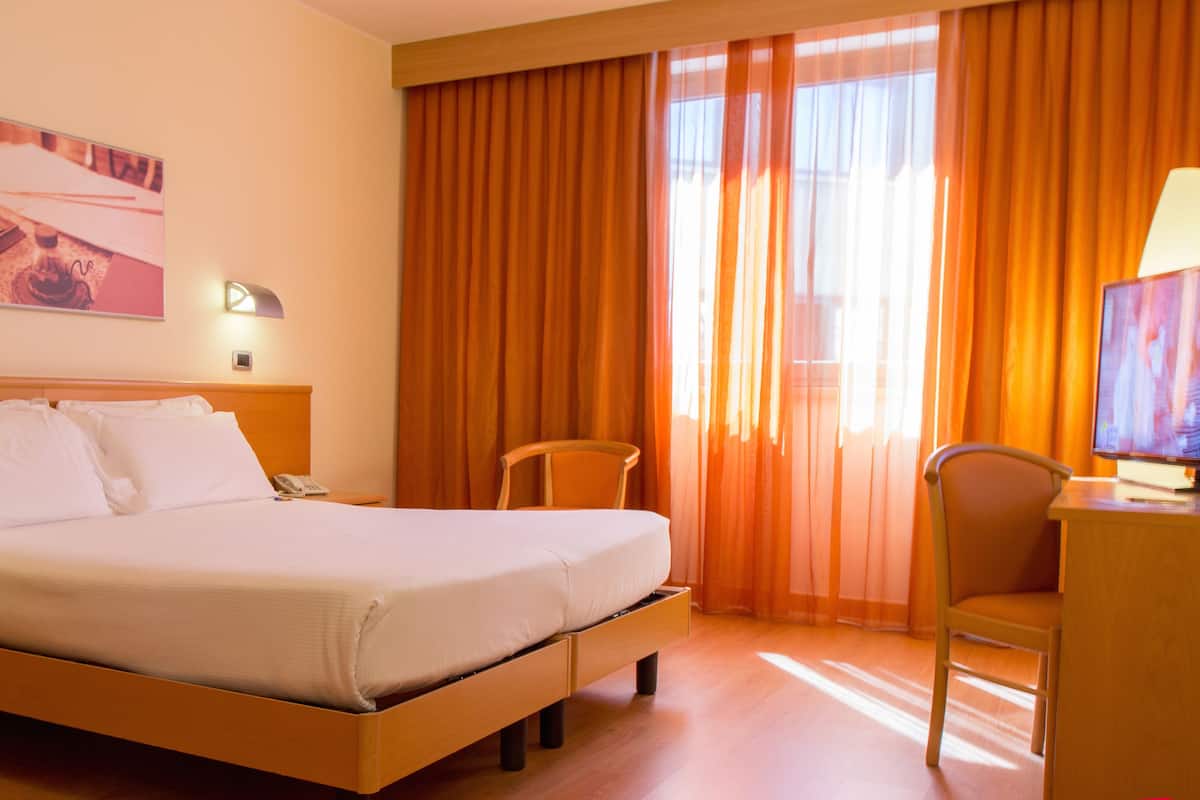Una habitación de hotel con una cama, un escritorio con lámpara, una silla y un televisor.