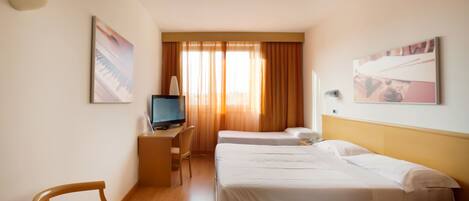 A hotel room with two beds, a desk with a television, and a chair.