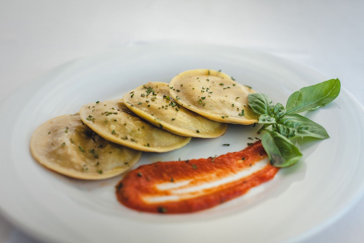 A plate with ravioli, a slice of tomato, and basil leaves.