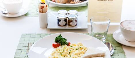 Un desayuno con huevos revueltos, tostadas y una guarnición de tomates en un plato blanco.