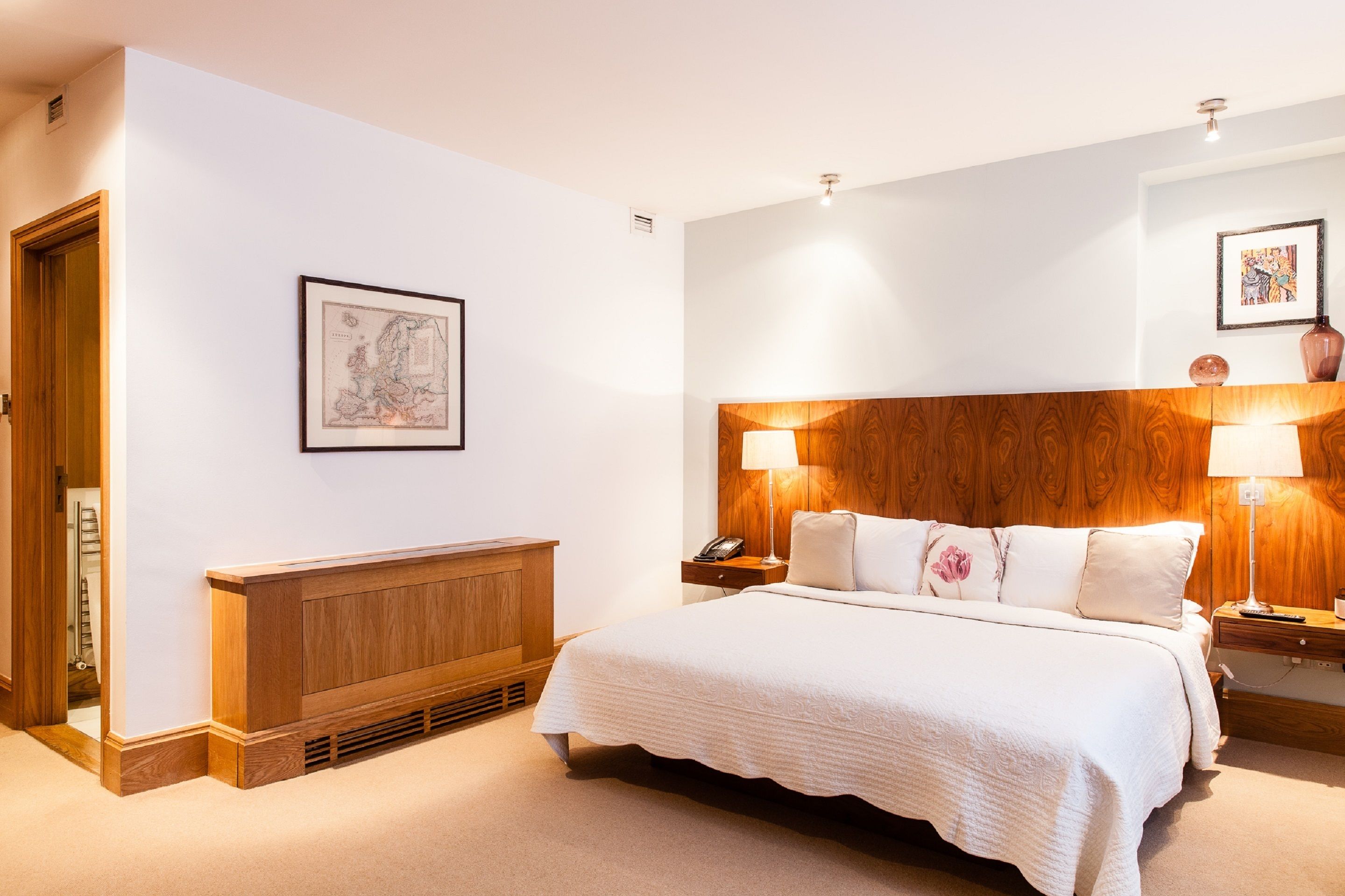 Een keurig opgemaakt slaapkamer met een groot bed, houten hoofdbord, bedlampen en een inlijsting kaart aan de muur.