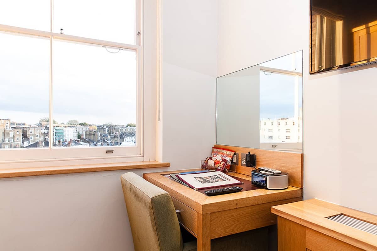 A small, modern room with a wooden desk, a chair, a large mirror, and a window overlooking a cityscape.