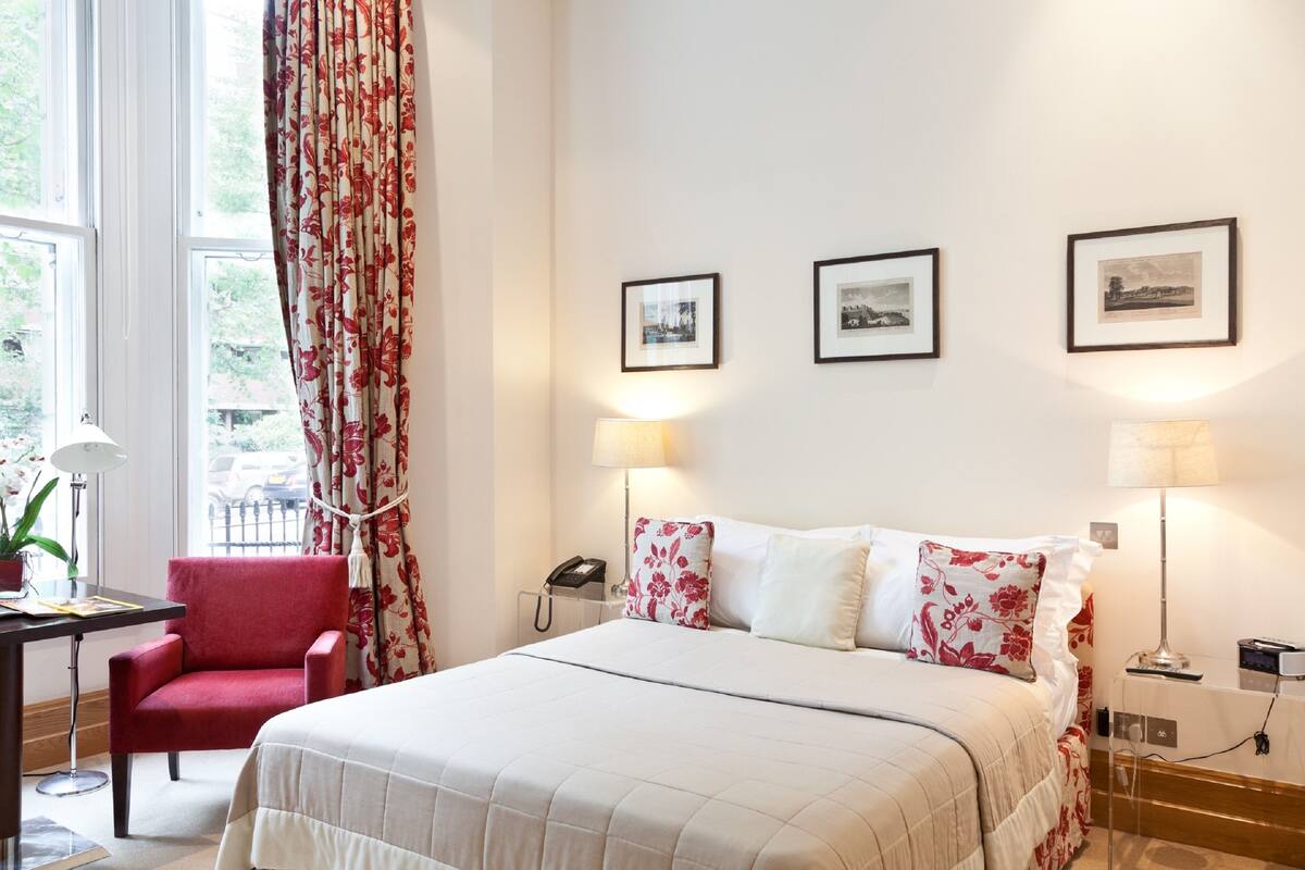 A hotel room with a bed, a desk, a chair, and a window with curtains.