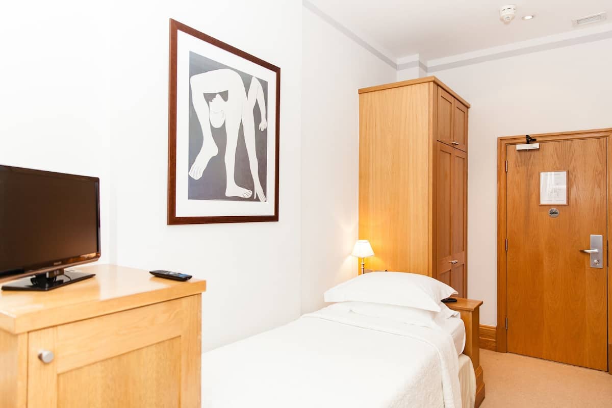 A hotel room with a bed, a TV on a wooden dresser, a wooden wardrobe, and a framed artwork on the wall.