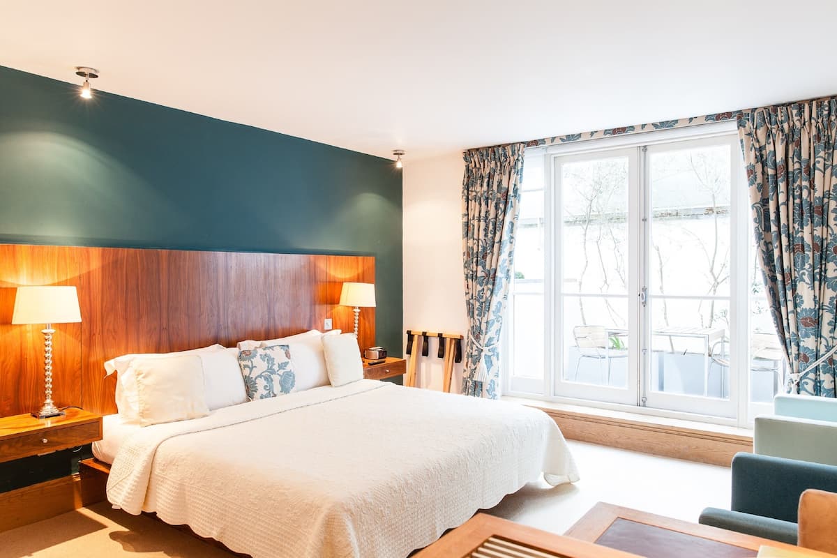 A hotel room with a large bed, two bedside lamps, a wooden headboard, a window with curtains, and a view of the outdoors.