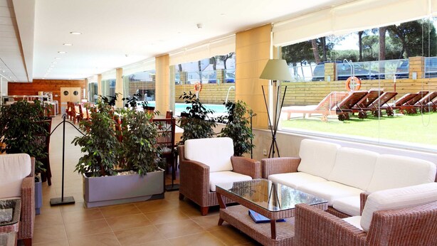 A spacious lobby with a white sofa, wicker chairs, a glass coffee table, and potted plants. - Vime Islantilla (Isla Cristina)
