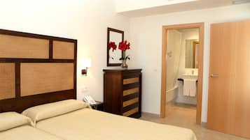 Hotelkamer met een bed, een houten dressoir, een vaas met bloemen, een telefoon, een spiegel, en een badkamer zichtbaar door een open deur.