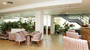 A spacious lobby with wicker furniture, a central table, and potted plants. - Vime Islantilla (Isla Cristina)