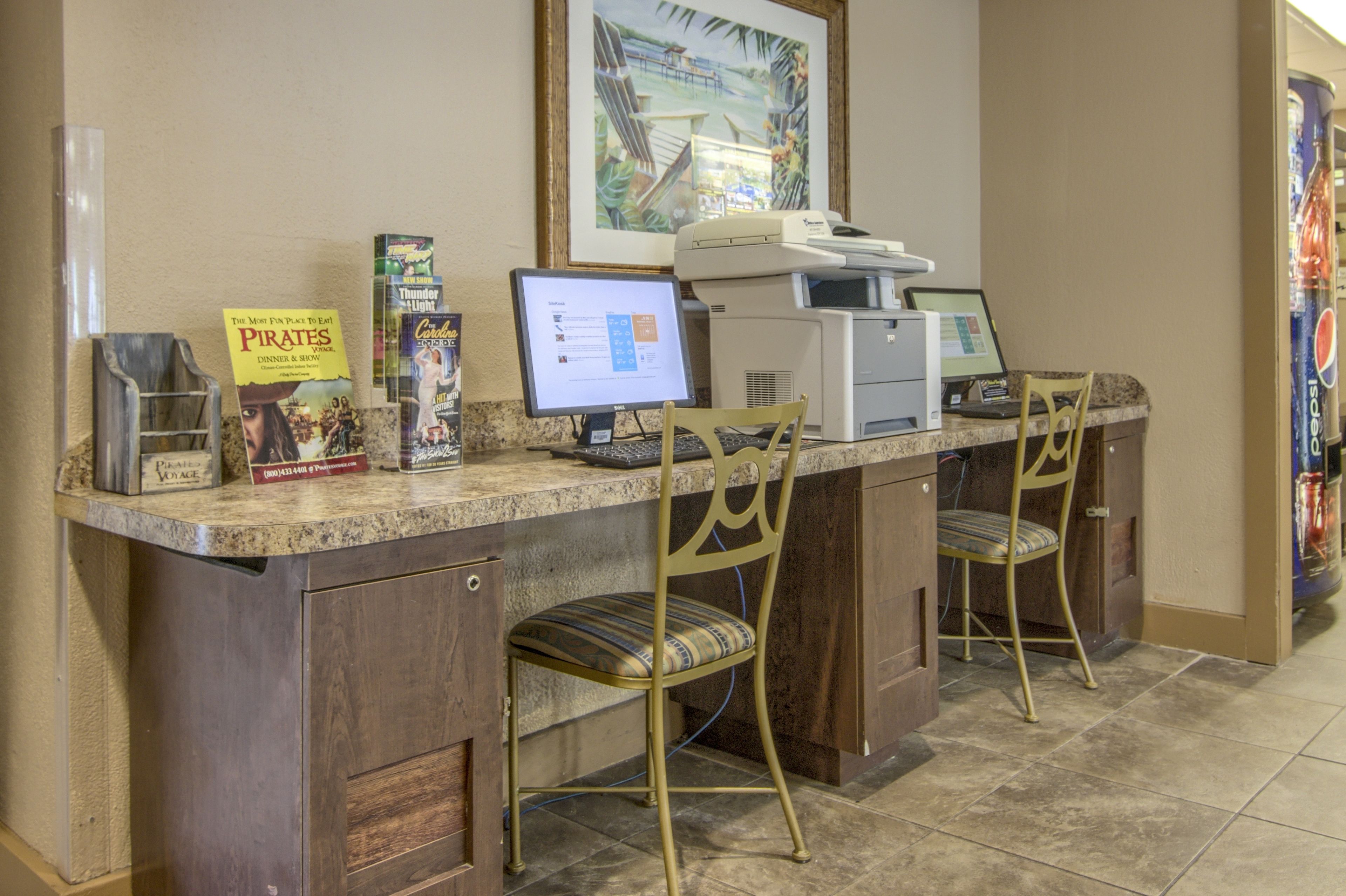 A reception desk with two computer monitors, a printer, and a framed picture on the wall. There are two chairs in front of the desk.