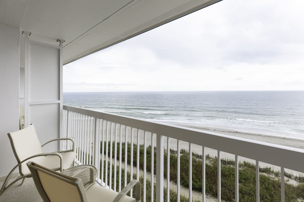 A balcony with a view of the ocean, white railings, and two chairs.