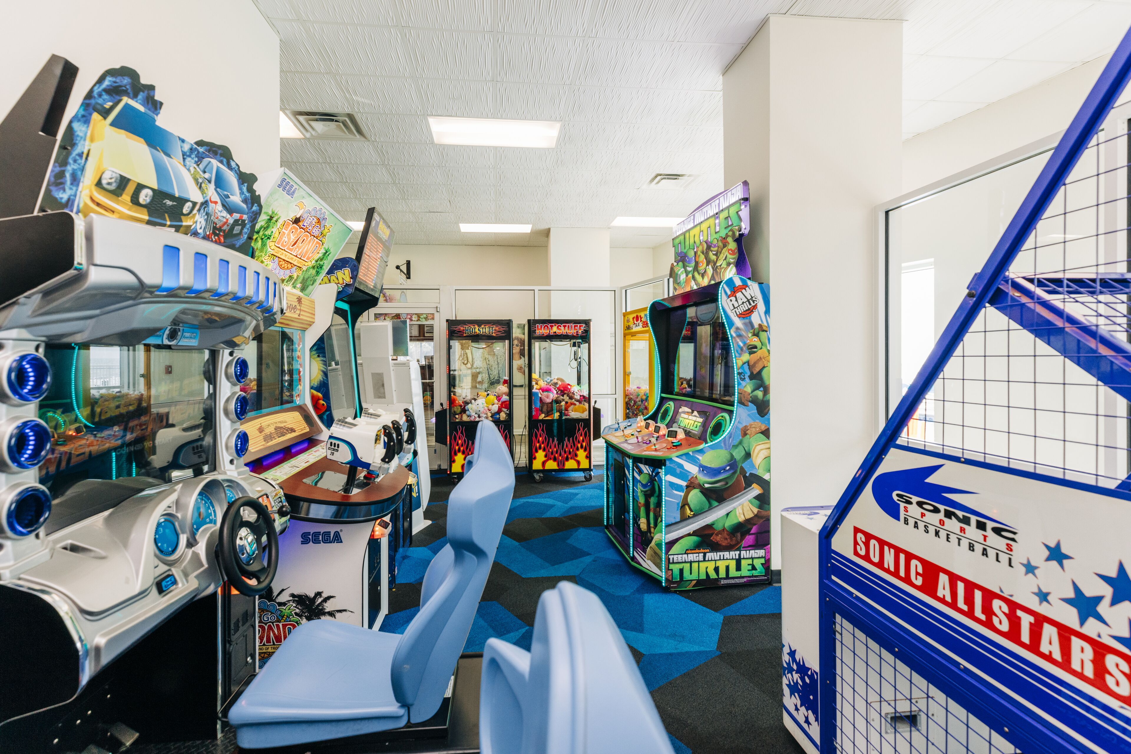 Una habitación con juegos de arcade, incluyendo un juego de carreras de SEGA y un juego de Tortugas, además de una cancha de baloncesto azul.