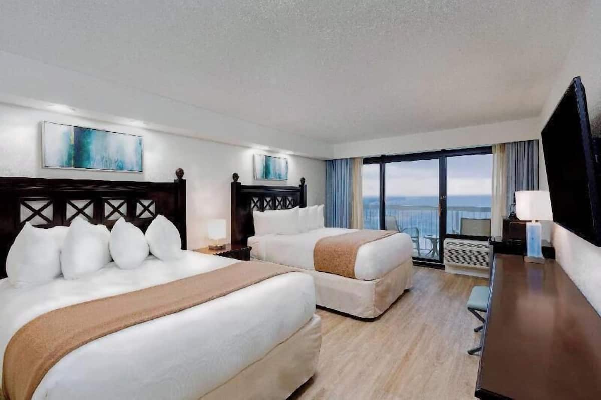 A hotel room with two beds, a desk, a chair, a TV, and a large window with a view.