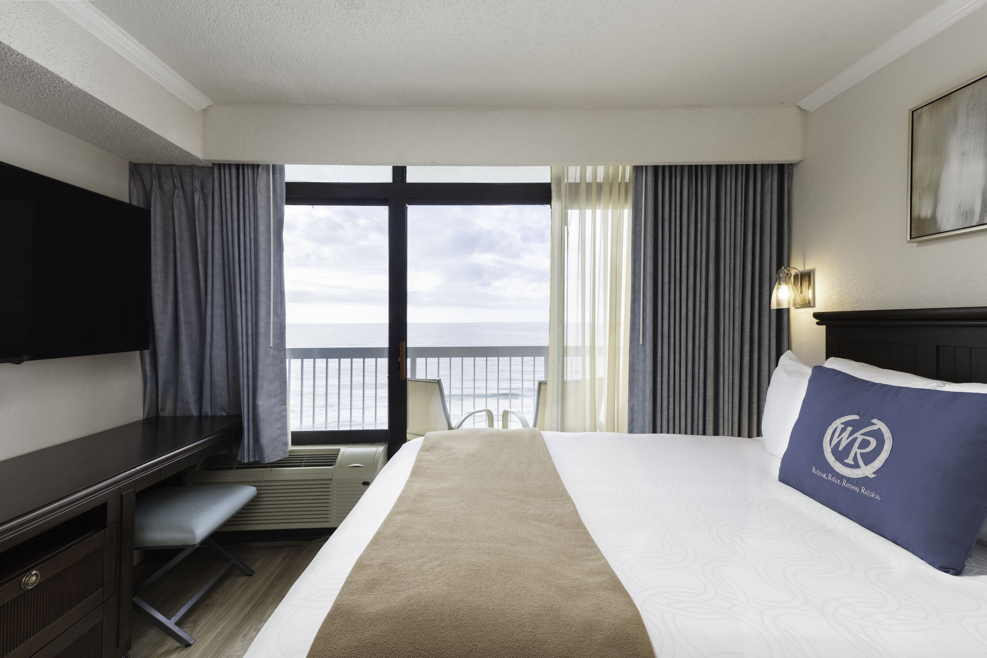 Et hotelværelse med seng, skrivebord, stol, fjernsyn og havudsigt.