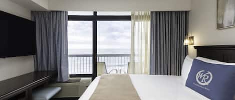 Et hotelværelse med seng, skrivebord, stol, fjernsyn og havudsigt.
