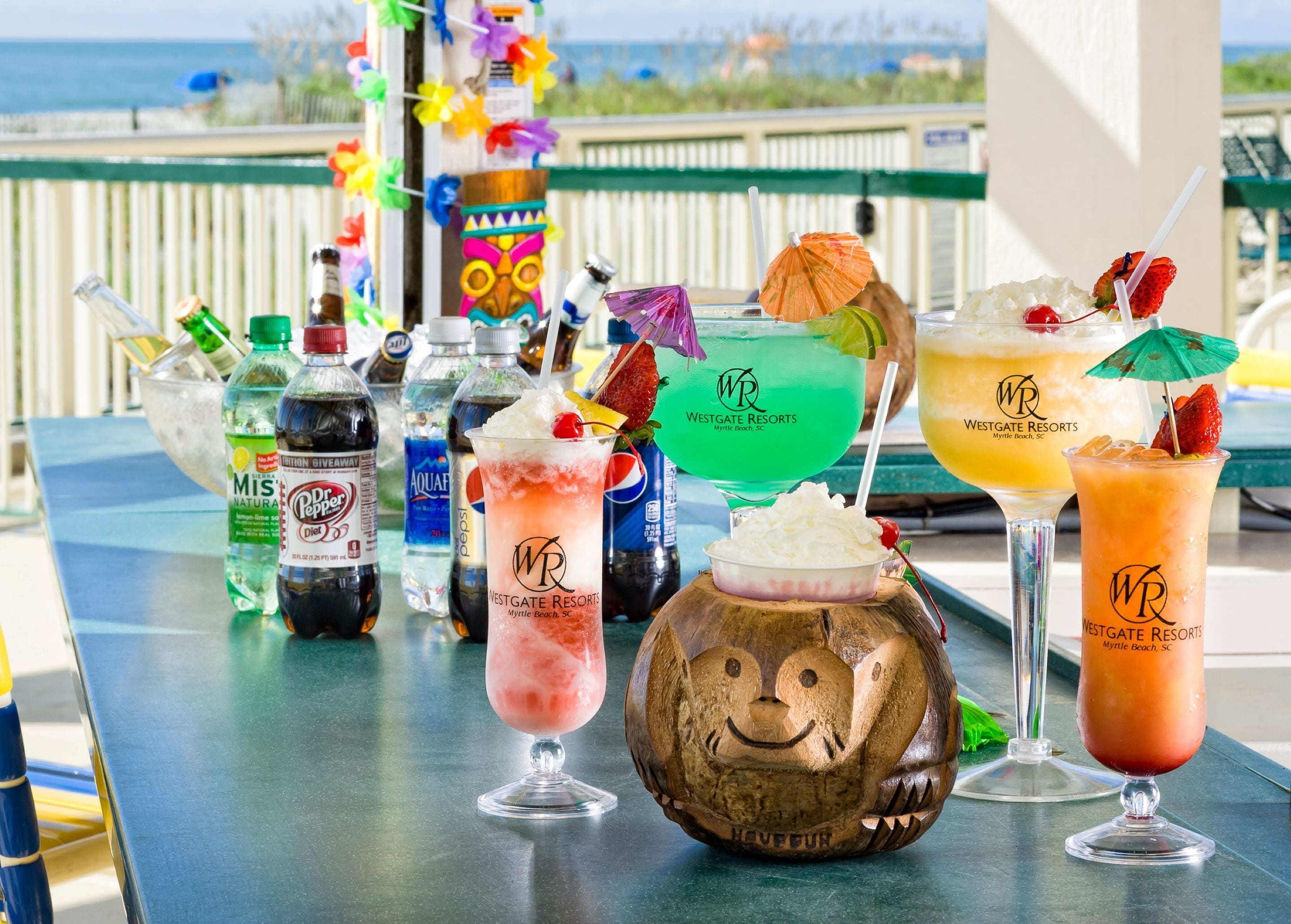 A variety of colorful cocktails on a table with a view of the beach in the background.
