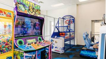 Zona de juegos recreativos con varias máquinas, incluyendo un juego de 'Teenage Mutant Ninja Turtles', y una zona de estar con sillas azules.