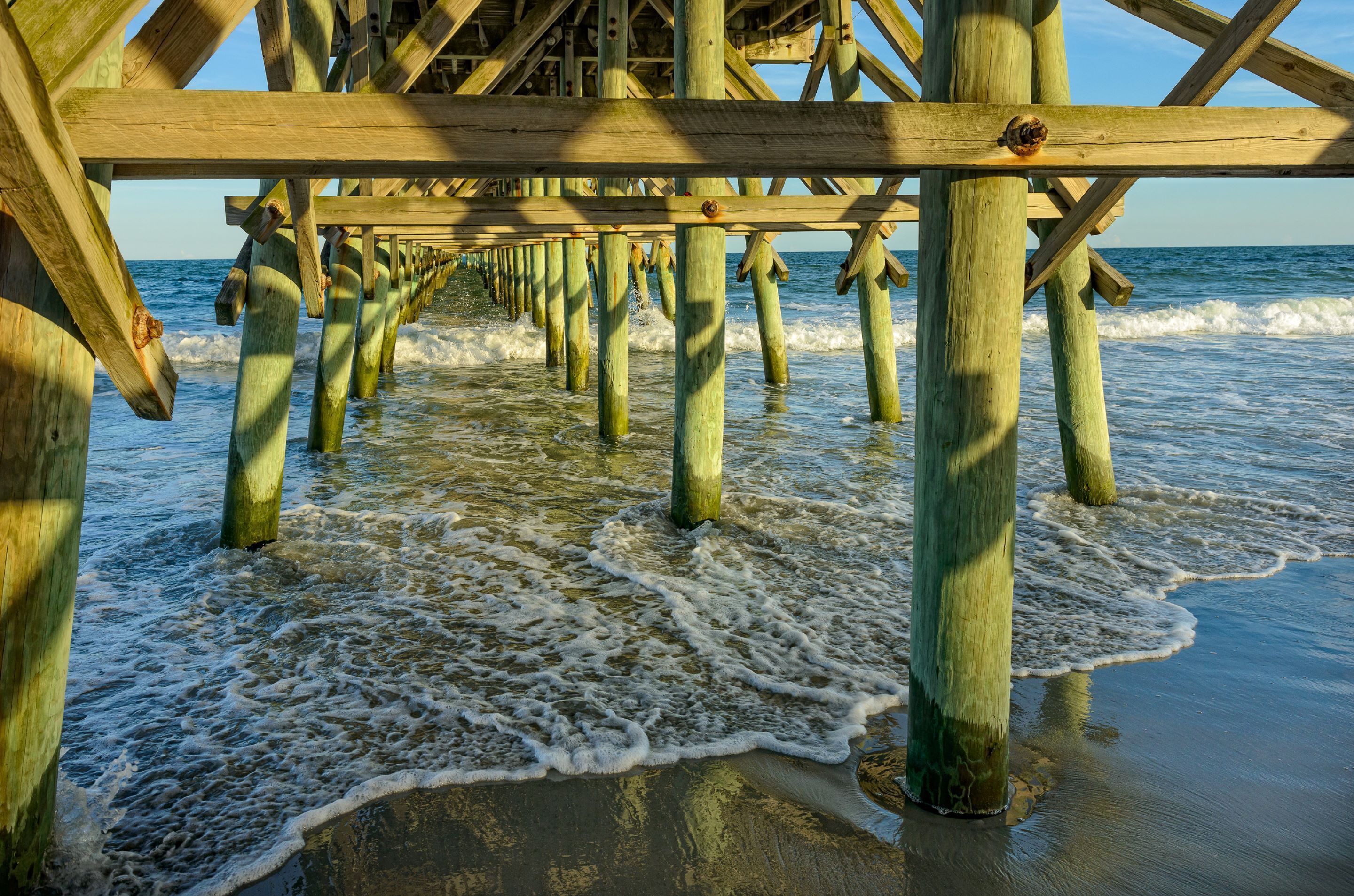 A wooden pier extending into the water with waves lapping at its base.
