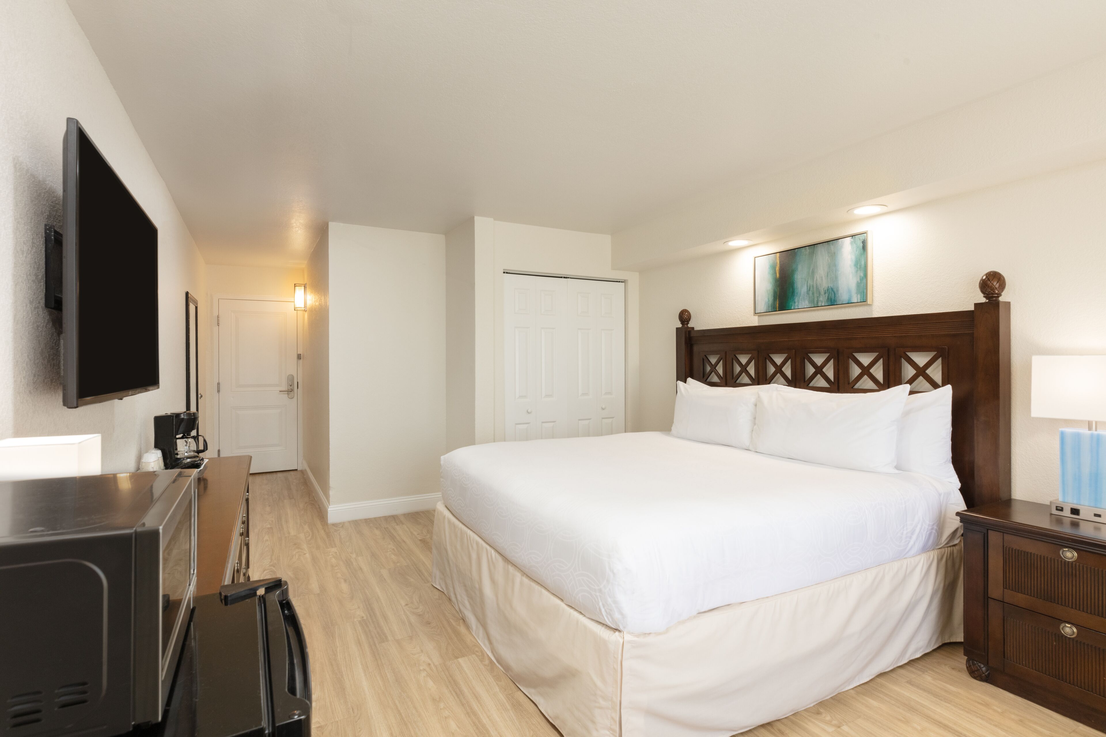 A hotel room with a large bed, a television, a coffee maker, and a wooden headboard.