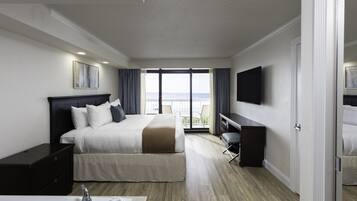 A hotel room with a bed, a desk, a TV, and a balcony with a view of the sea.