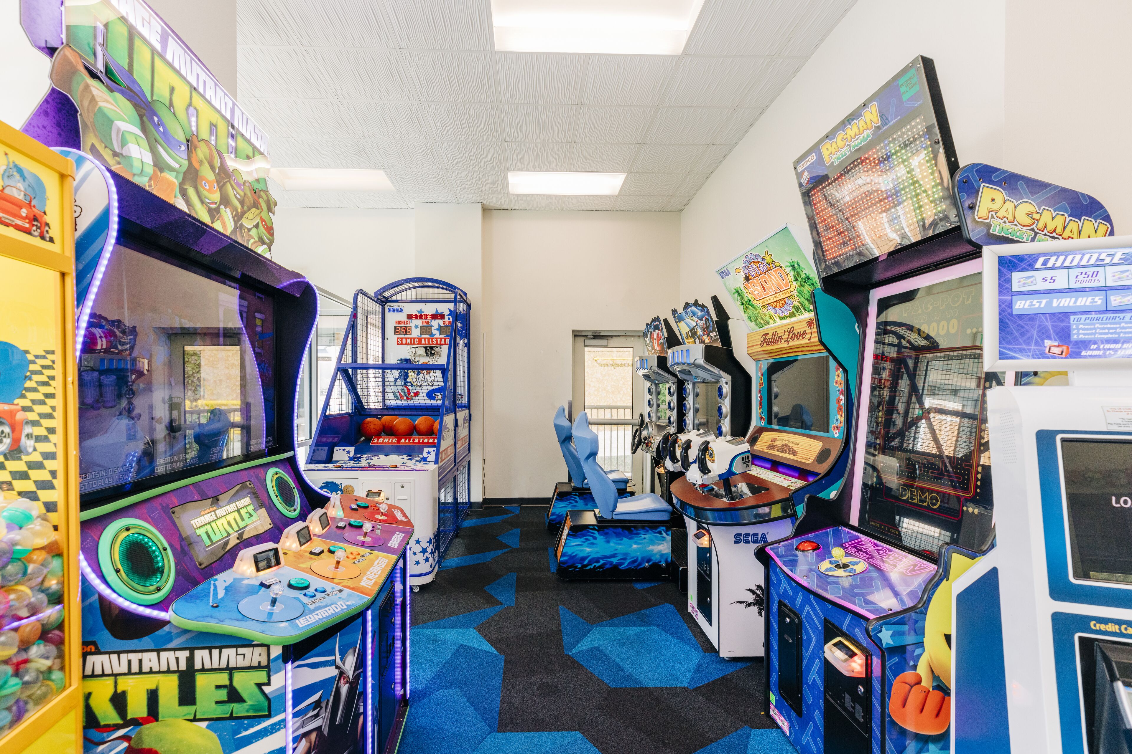A row of arcade games in a brightly lit room with a checkered floor pattern.