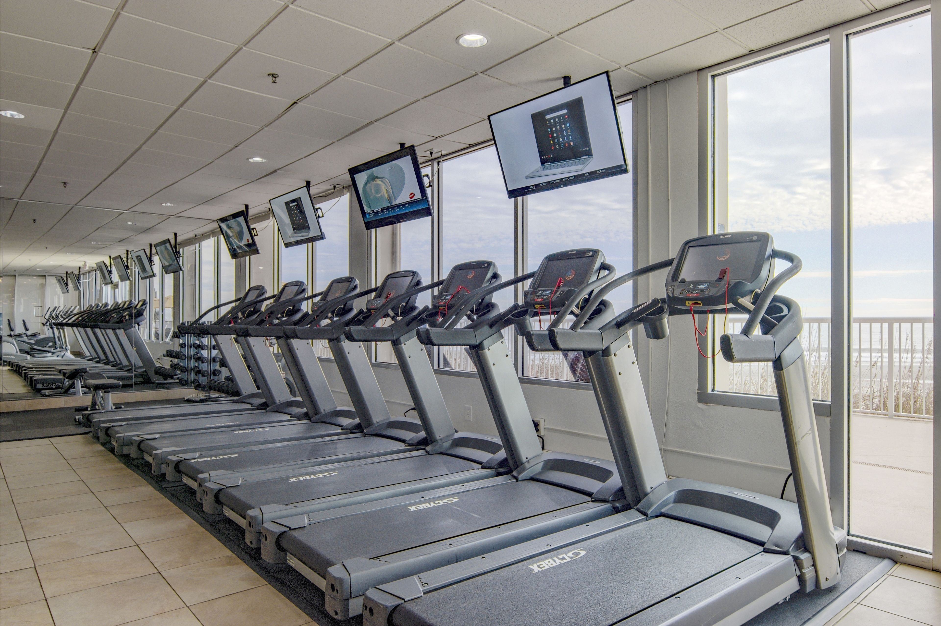 Eine Reihe von Laufbändern in einem Fitnessstudio mit großen Fenstern und Blick zum Himmel.