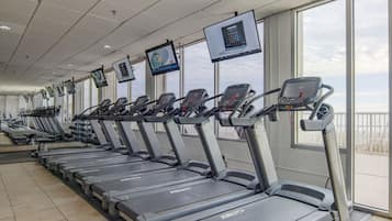 File di tapis roulant in una palestra con ampie finestre e vista sul cielo.