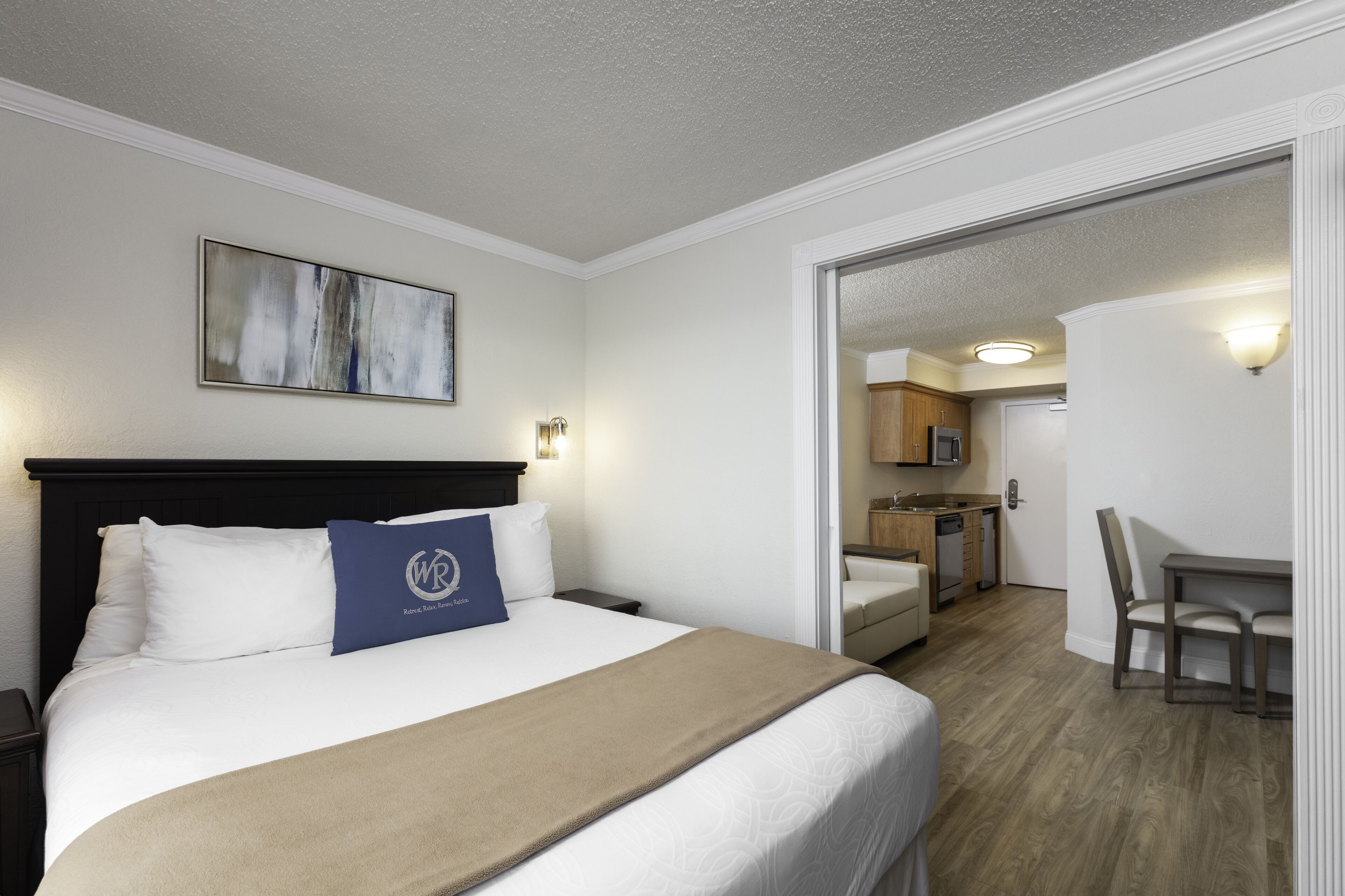 Une chambre d’hôtel avec un lit, un tableau, un bureau et une kitchenette.