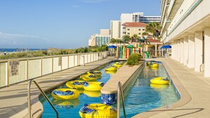 En pool med flera uppblåsbara badringar, en skylt med information om badvakten och utsikt över havet.