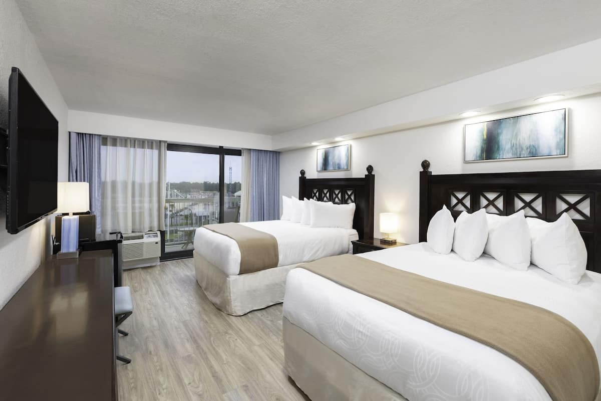 A hotel room with two beds, a TV, a desk, and a view of a cityscape.