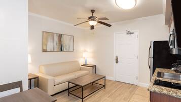 A modern living room with a beige sofa, a coffee table, a ceiling fan, and a kitchen area with a sink and stove.