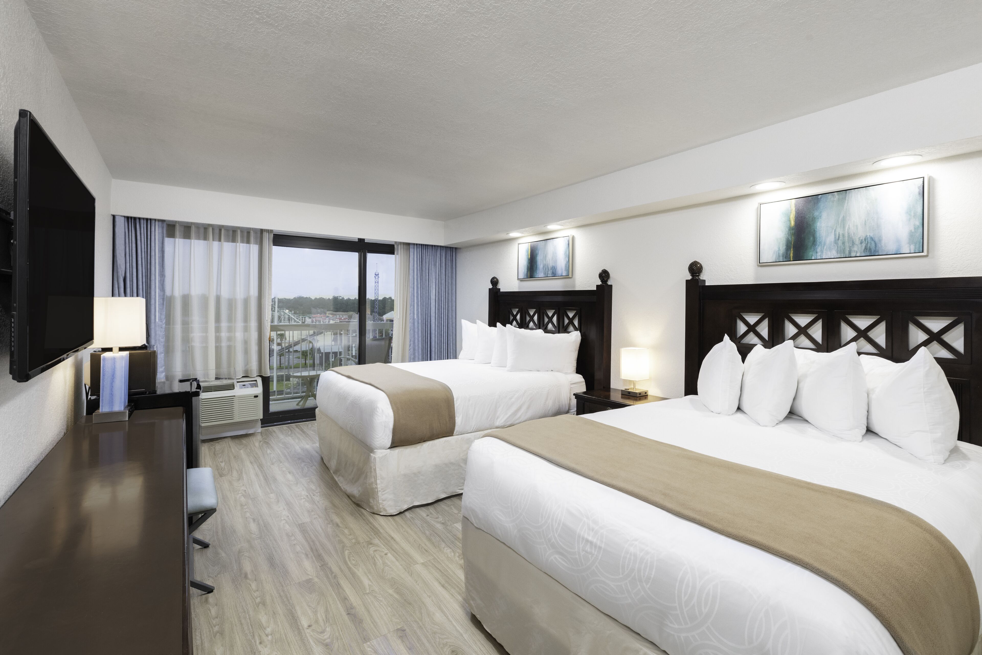 Ein Hotelzimmer mit zwei Betten, einem Schreibtisch, einem Fernseher und einem Fenster mit Blick auf die Stadt.