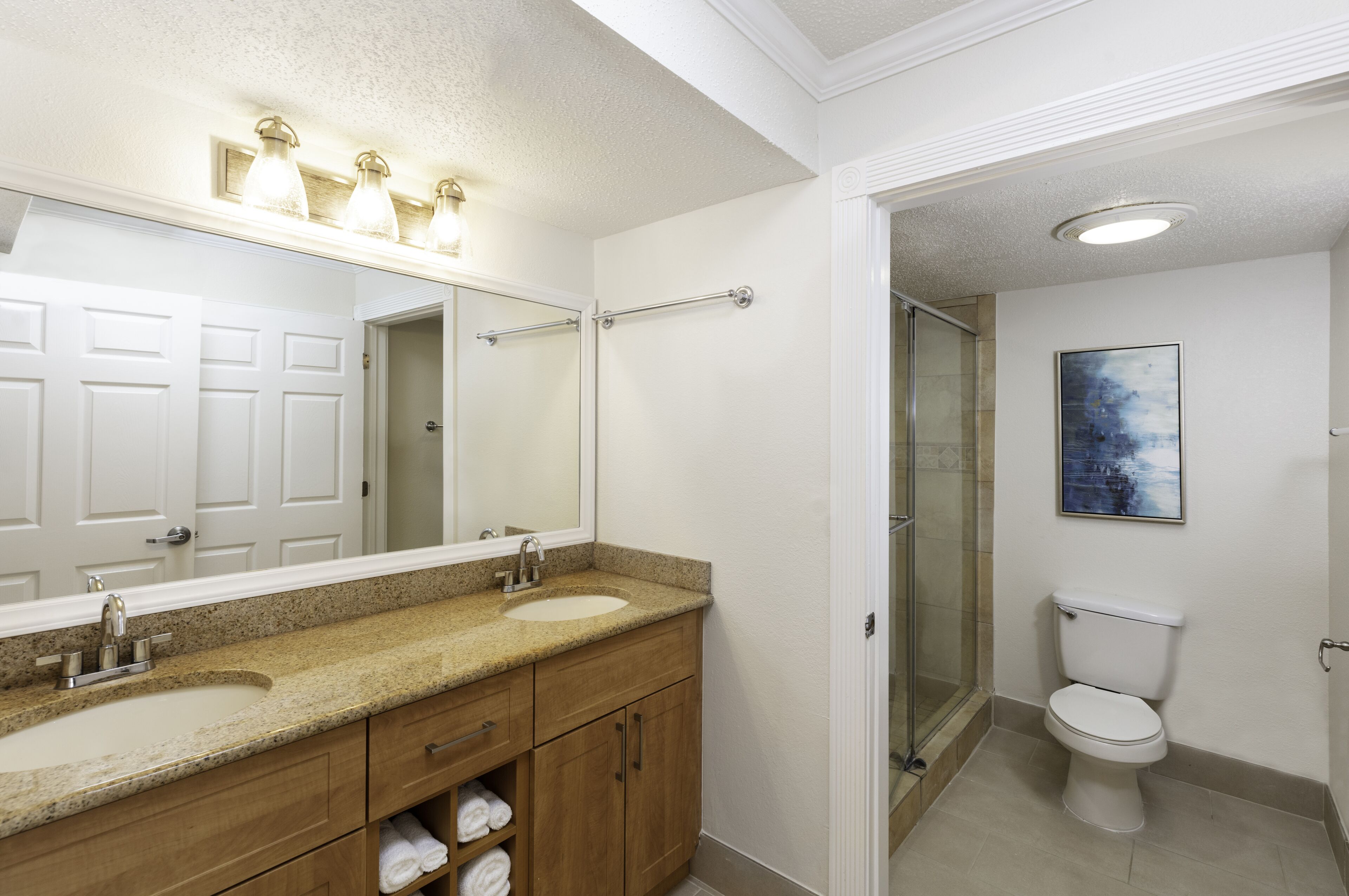 A bathroom with a double sink vanity, a large mirror, a shower with a glass door, and a toilet.