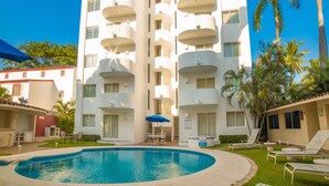 Un hotel de varios pisos con piscina, mobiliario exterior y palmeras.