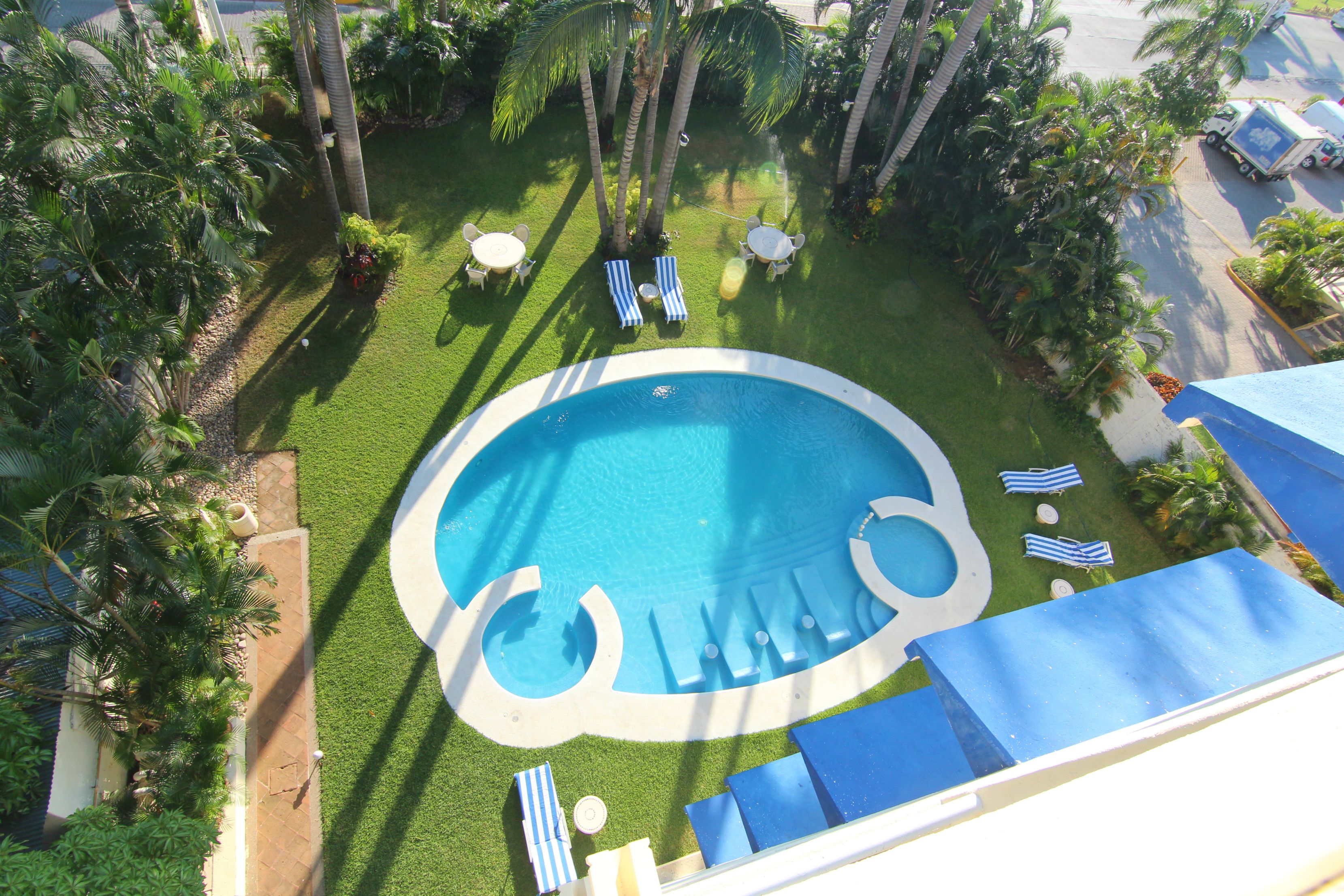 Una piscina con sillones de descanso y un jardín de palmeras.