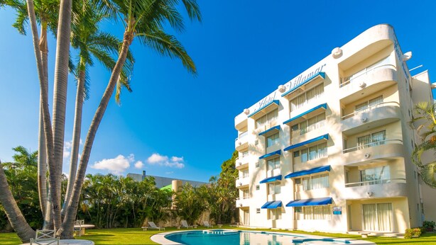Un hotel con piscina, palmeras y un cielo azul despejado.