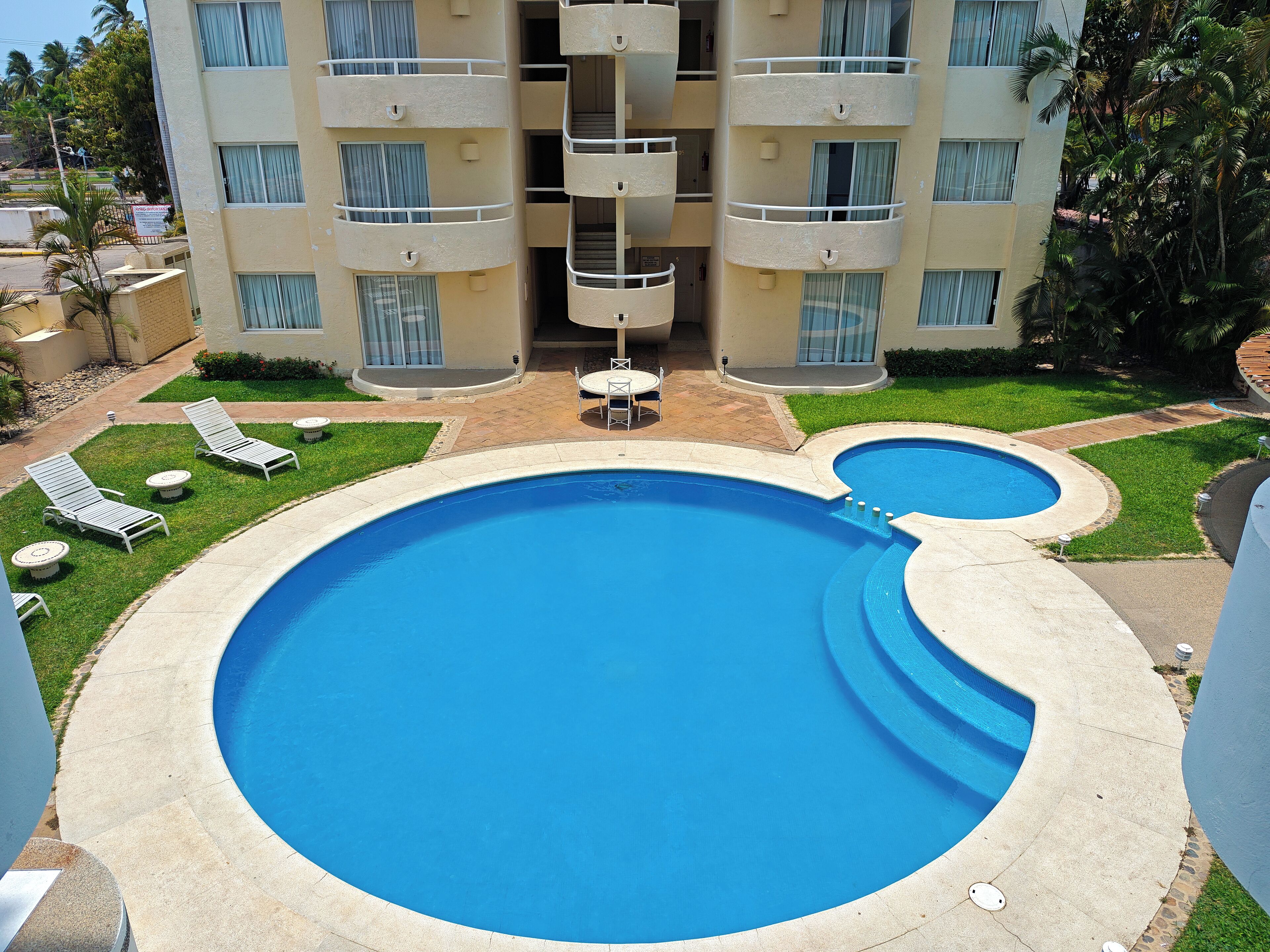 A swimming pool with a curved design, surrounded by a patio area with lounge chairs and a table.