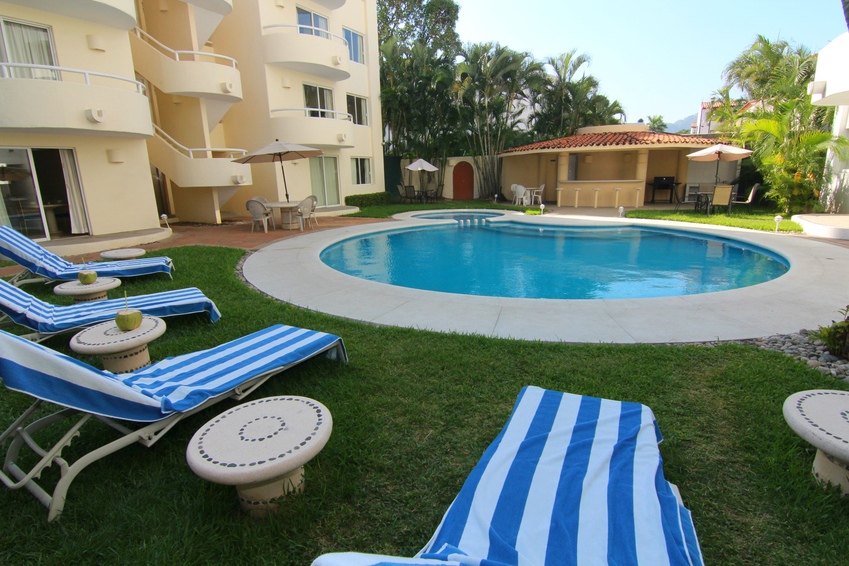 A pool area with lounge chairs and umbrellas, surrounded by a building with balconies and a covered patio.