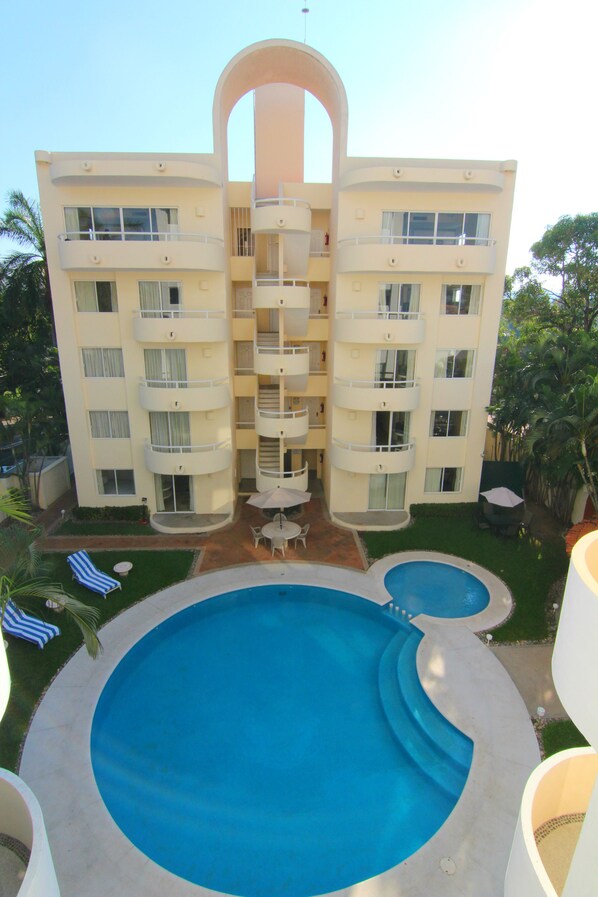 A multi-story hotel with a central courtyard featuring a large swimming pool, outdoor seating, and lush greenery. - Hotel Villamar Princesa Suites (Acapulco)
