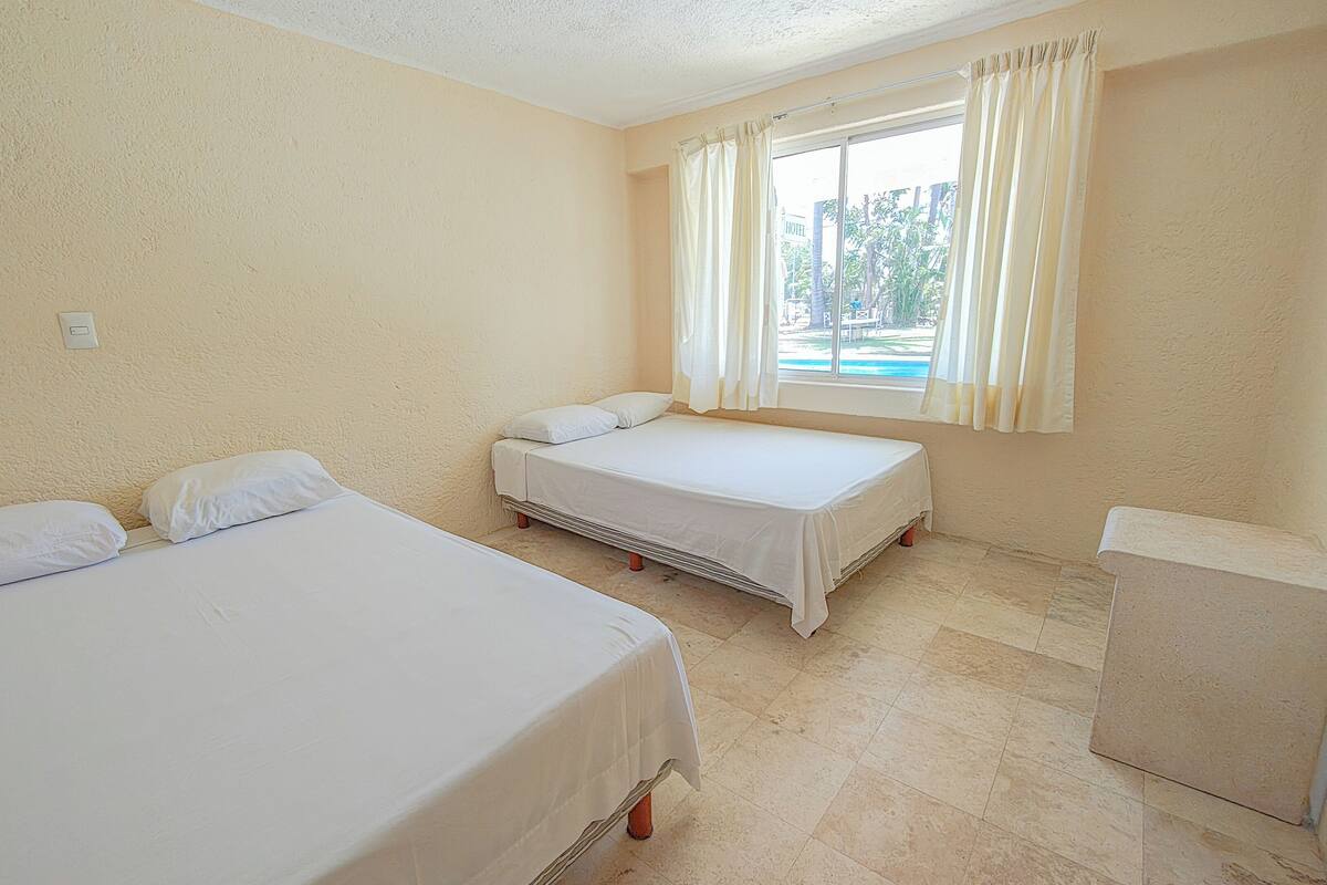 A room with two single beds, a window with curtains, and a small desk.