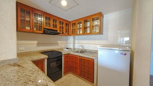 Una cocina compacta con armarios de madera, una estufa a gas, un lavamanos y un refrigerador blanco.